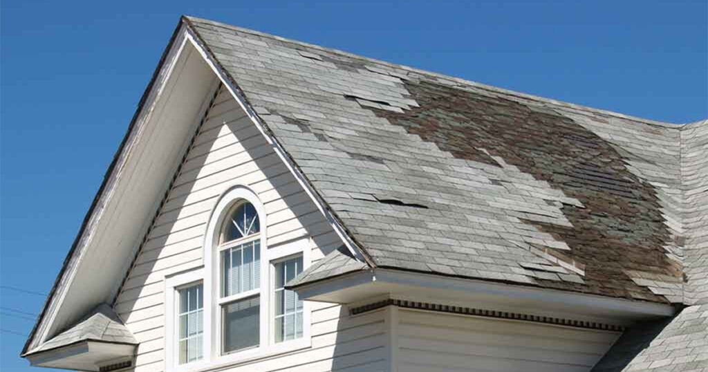 Old deteriorated roof suffered from wind damage with fallen shingles and exposed plywood.