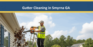 A worker in a green safety vest and cap is on a ladder, using an orange leaf blower to clear a large amount of brown leaves from the gutters of a white residential house. A pile of leaves is on a tarp below, with other suburban homes and trees in the background under a sunny sky. The image features a badge blue banner at the top with "Gutter Cleaning in Symna GA" in white text, bordered by canary yellow.