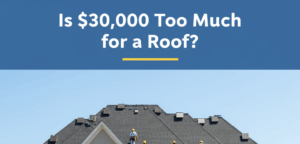 A large crew of roofers in yellow hard hats and white uniforms are actively working on installing a new dark grey shingle roof on a grand, light grey two-story house. Scaffolding is set up on the left side, and a yellow dumpster, a yellow pickup truck, and stacks of roofing materials are on the driveway and lawn.